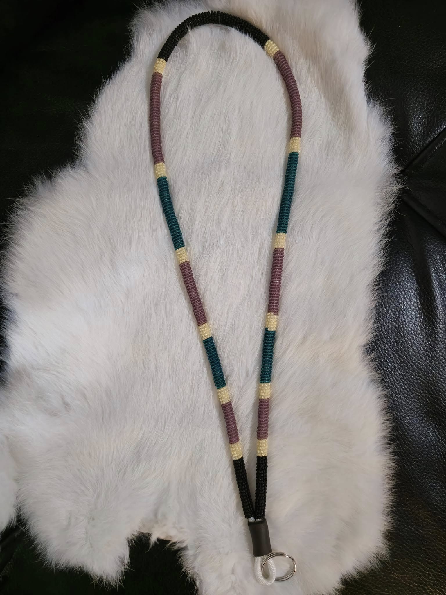A hand-beaded lanyard in black, cream, plum, and teal